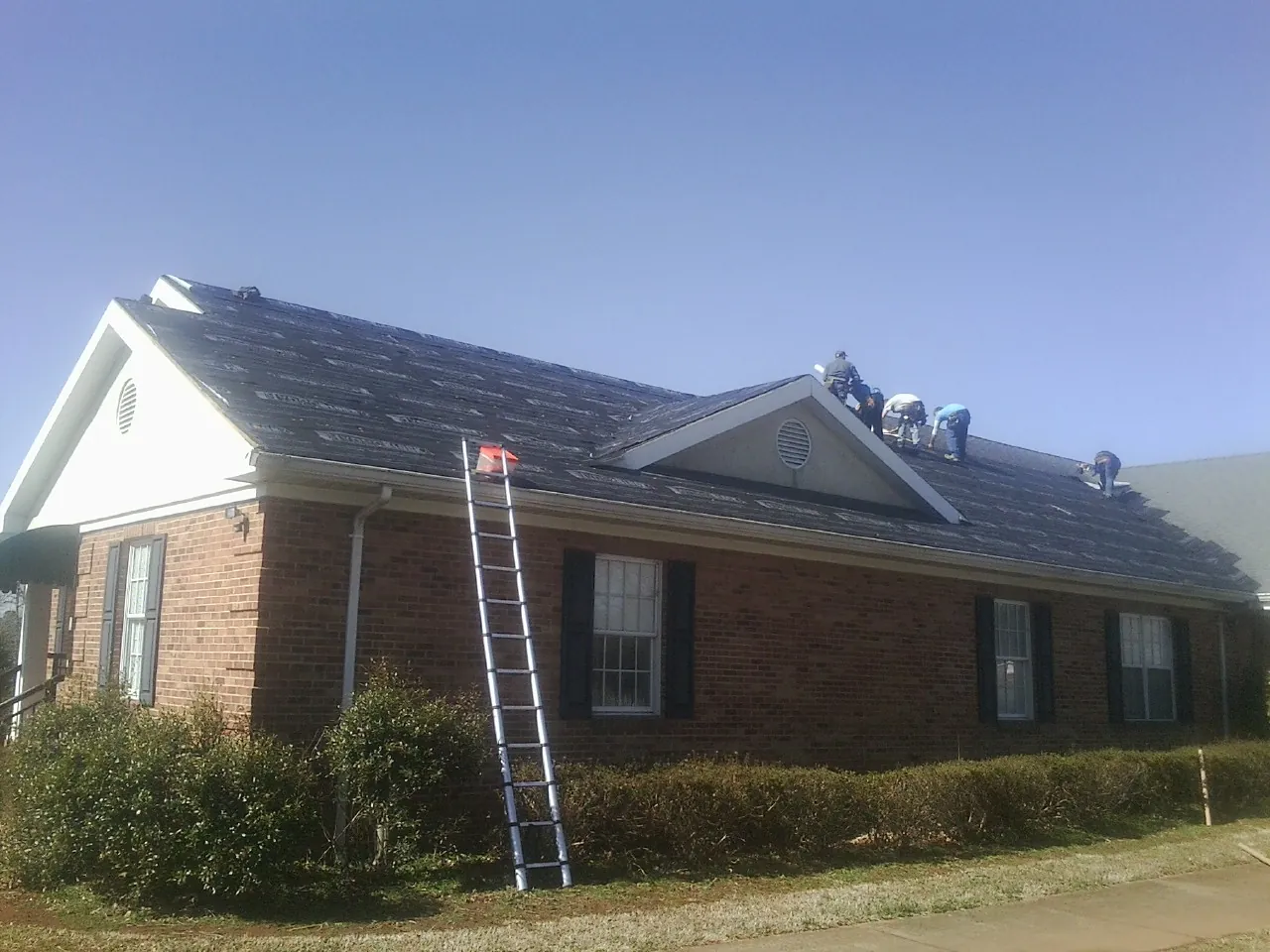 Crew tearing shingles off a brick ranch roof with a ladder set — Metal Roof Repair work by our crew in Bolivar