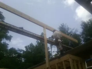 Carpenter setting a ridge beam over a new addition frame in Bolivar