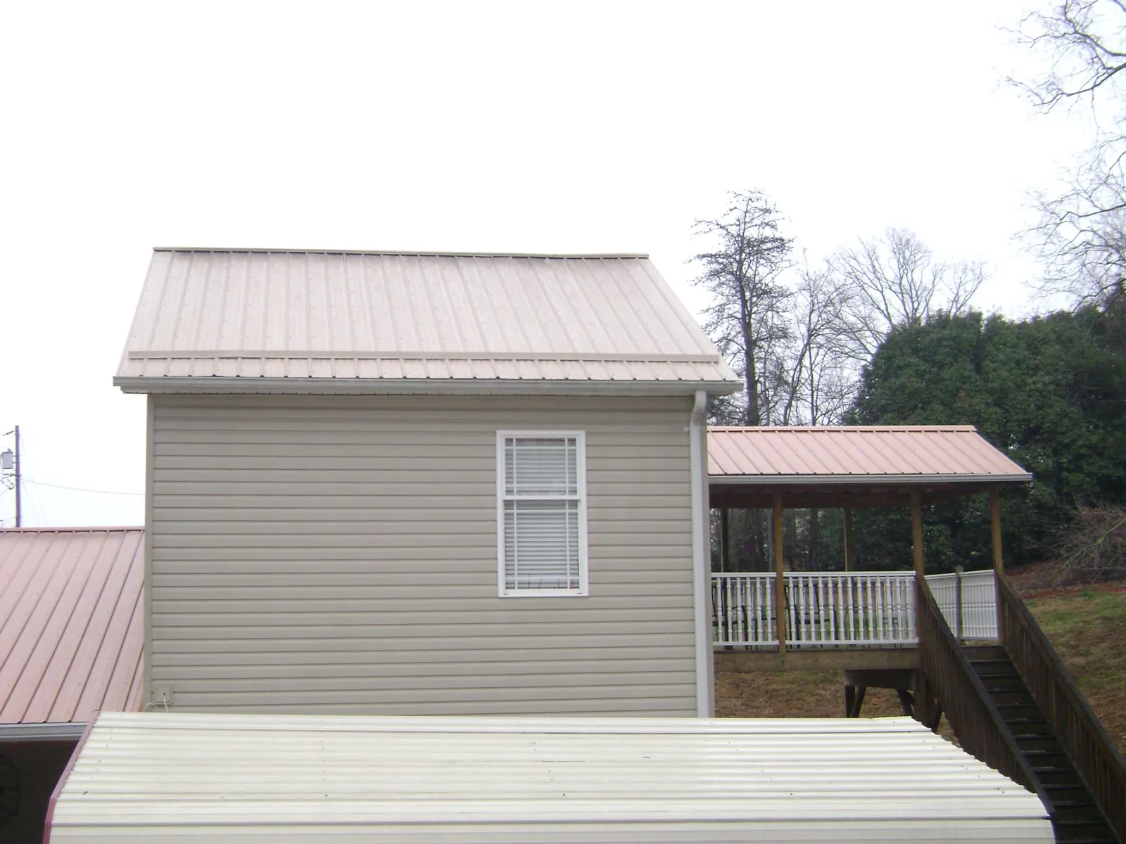 Tan metal roofs on a two story addition and attached porch, from a Roof Replacement job in Bolivar